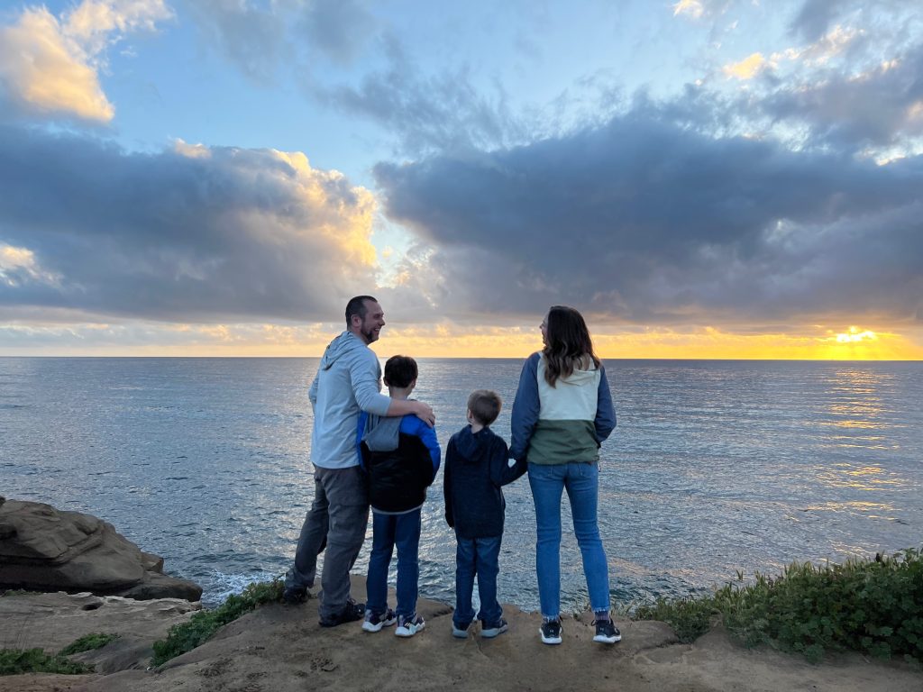 Father, mother, and two boys standing on a cliff overlooking the ocean in San Diego